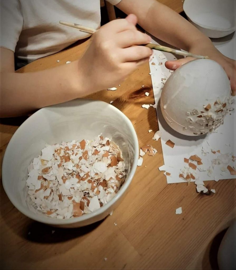Dziecko okleja styropianowe jajo skorupkami prawdziwego jajka