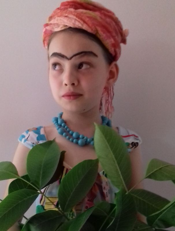 Dziewczynka w turbanie na głowie z dorysowanymi brwiami trzyma zieloną roślinę