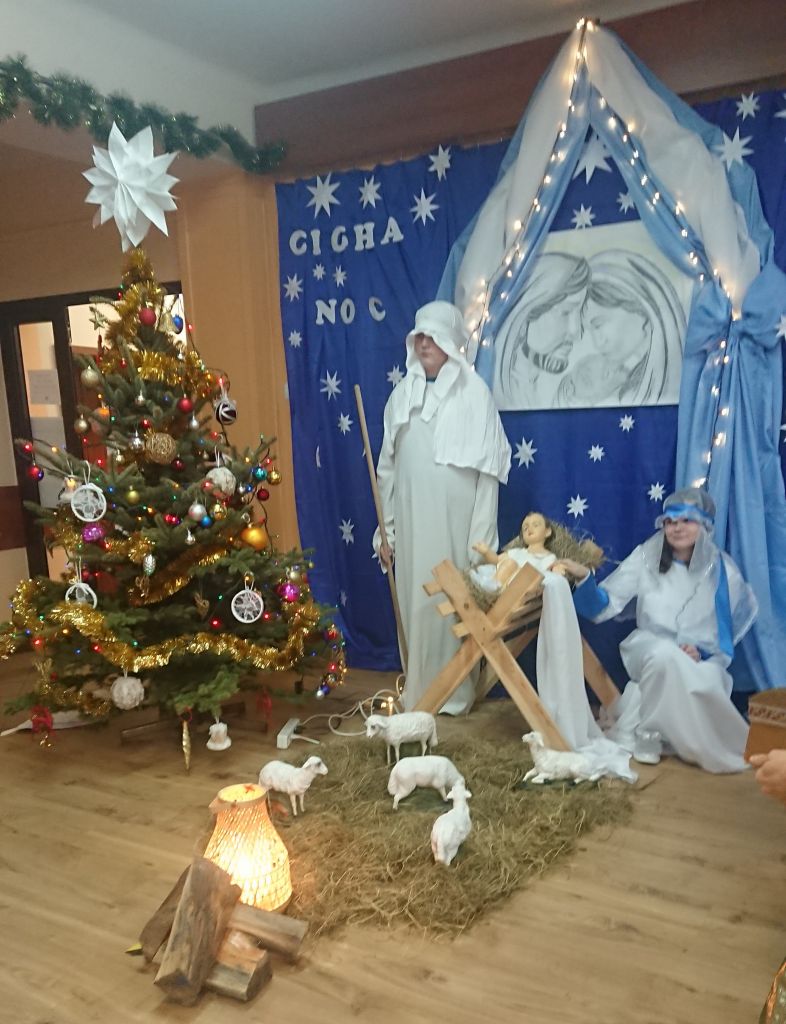 Szkolne jasełka - uczniowie w białych szatach, świąteczne dekoracje na scenie